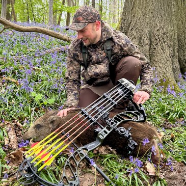 Chasseur à l'arc auprès d'une bête rousse dans un sous-bois couvert de jacinthes sauvages