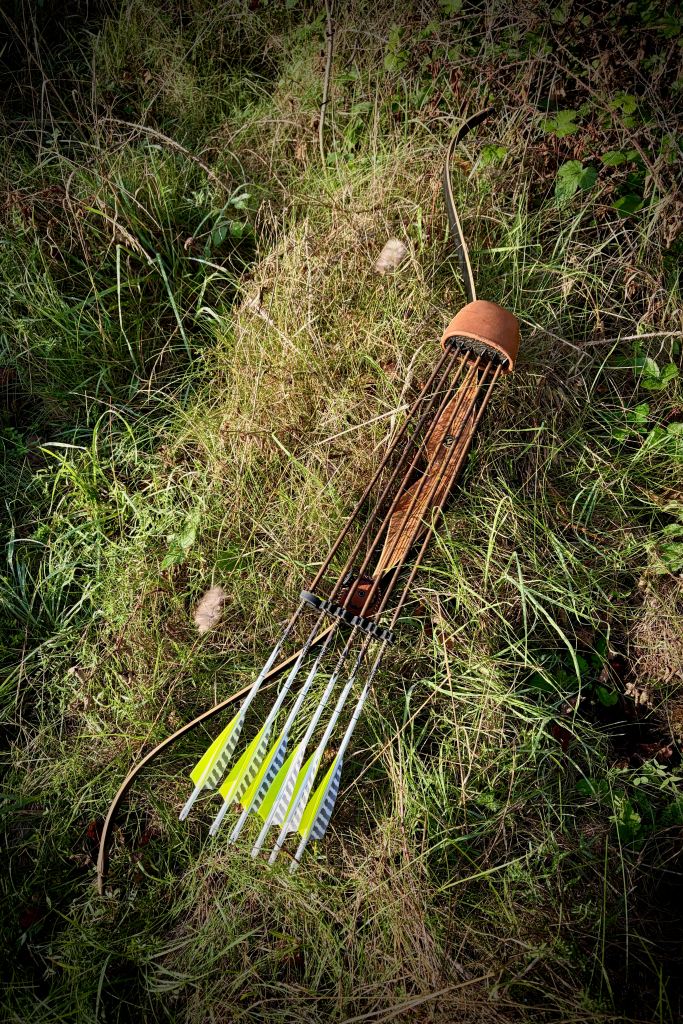 Arc traditionnel et carquois de flèches aux empennages jaunes fluorescents, posés dans la végétation en forêt