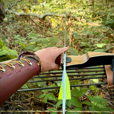 Vue à la première personne d'un arc traditionnel avec une flèche encochée dans une végétation forestière dense